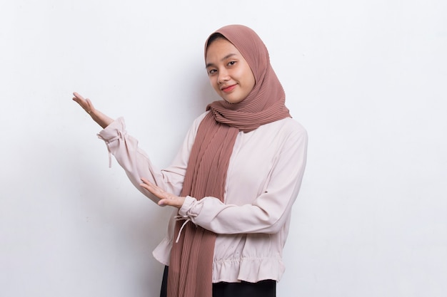 Happy young asian muslim woman pointing with fingers to different directions on white background