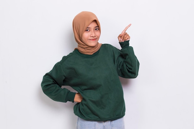 Happy young asian muslim woman pointing with fingers to different directions on white background