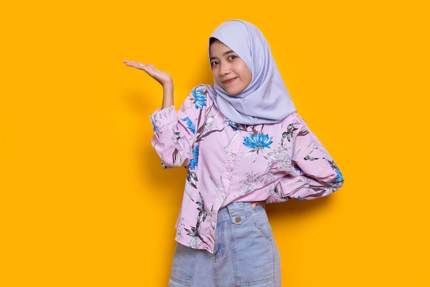 Happy young asian muslim woman pointing with fingers to different directions on yellow background