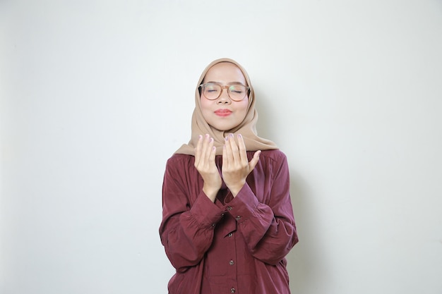 Счастливая молодая азиатская мусульманка в очках молится обеими руками