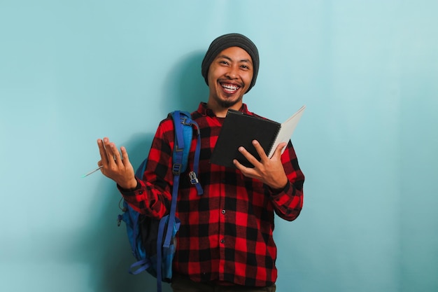 Happy young Asian student is smiling at the camera while standing against a blue background