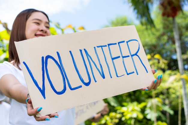 Happy young Asian students diverse volunteers hold a campaign sign for cleaning in the park The concept of environmental conservation on world environment day recycling charity for sustainability