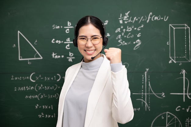Happy young asian teacher woman showing fist fighting sign\
video conference with student looking camera female teacher\
training the mathematics in classroom blackboard online course