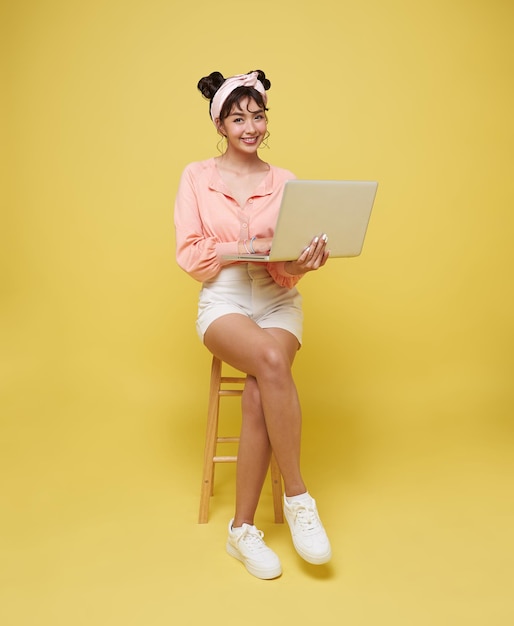 Happy young Asian teen woman smiling While her using laptop sitting on white chair