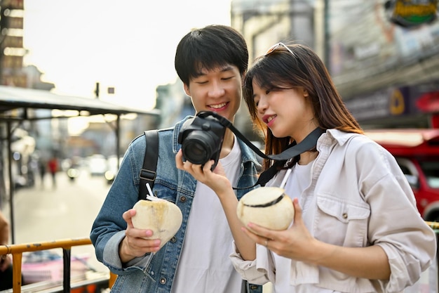 Happy young Asian tourist couple checking their photos on camera while sightseeing the city