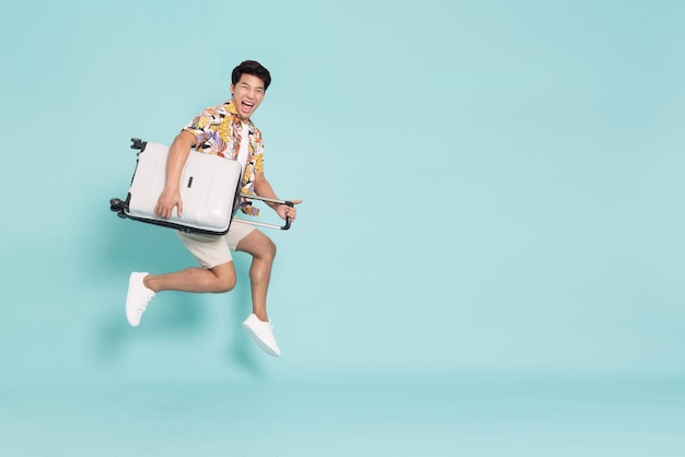 Happy Young Asian traveler man jumping with suitcase bag isolated on green background