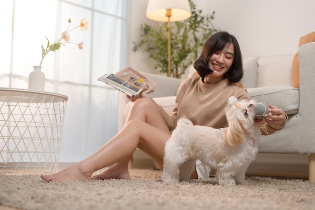 행복한 젊은 아시아 여성이 거실에서 귀여운 개와 함께 애정을 나누고 시간을 보내고 있습니다.