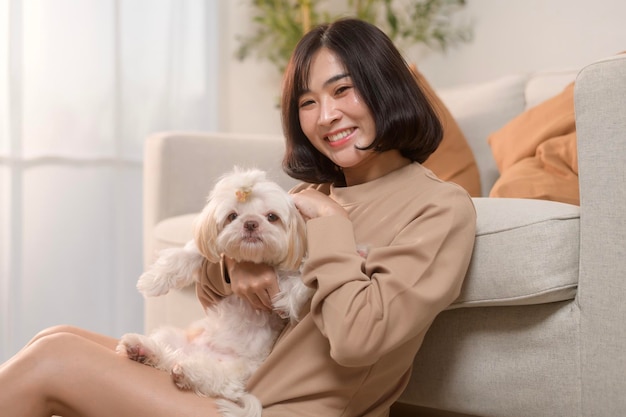 행복한 젊은 아시아 여성이 거실에서 귀여운 개와 함께 애정을 나누고 시간을 보내고 있습니다.