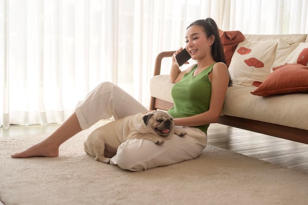행복한 젊은 아시아 여성이 거실에서 귀여운 개와 안고 시간을 보내고 있습니다.