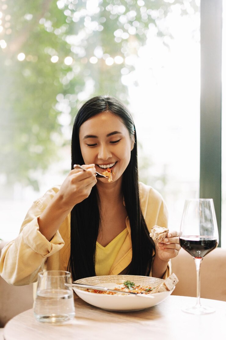 Photo 幸せな若いアジア人女性がレストランで赤ワインを食べ飲んでいます