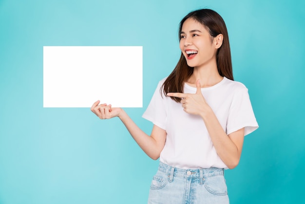 Felice giovane donna asiatica in possesso di un foglio bianco con la faccia sorridente e guardando lo sfondo blu. per insegne pubblicitarie.