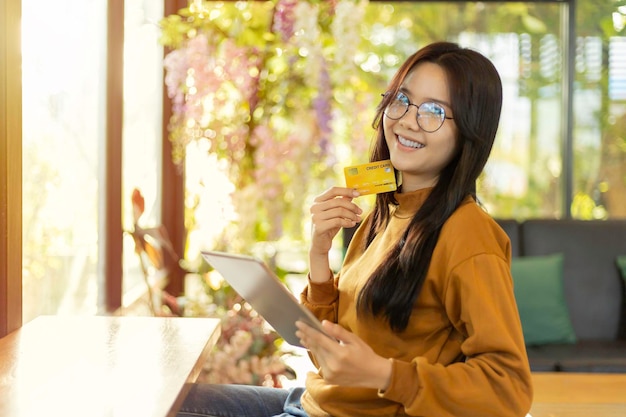 Happy young asian woman holding credit card and tablet for electronic payment in internet online remote store
