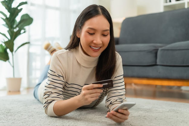 Felice giovane donna asiatica in possesso di carta di credito e utilizzando smartphone per lo shopping online con il pagamento su internet banking