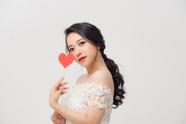 Happy young Asian woman holding love sign over white background