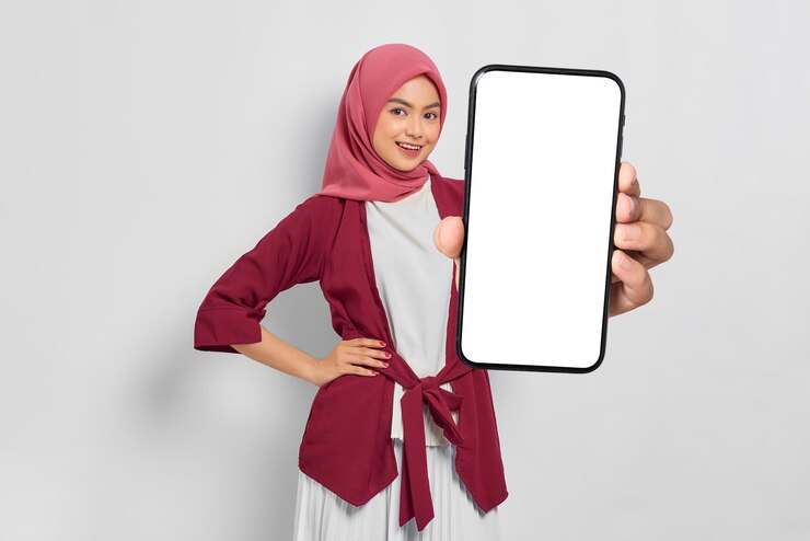 白い背景に隔離された白い画面のスマートフォンを握っている幸せな若いアジア人女性