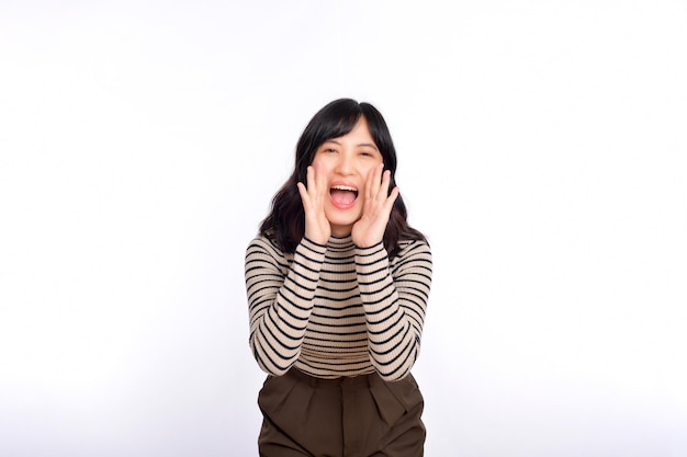 Happy young asian woman professional entrepreneur standing in casual clothing open mouths raising hands shout announcement white background