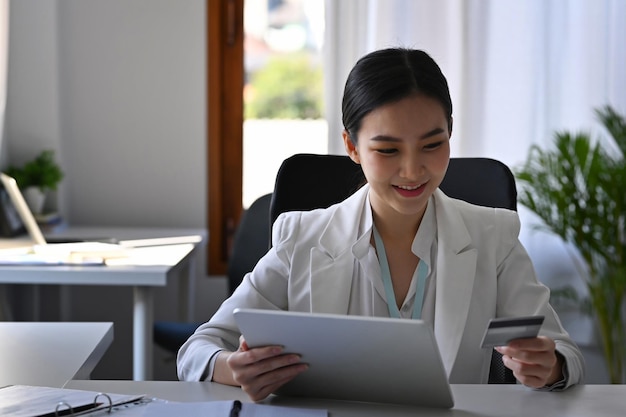 幸せな若いアジアの女性がデジタルタブレットを介してオンラインショッピング。