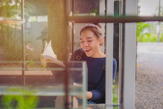 カフェと読書のテーブルに座っている幸せな若いアジアの女性。