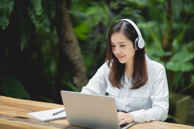 Happy young asian woman smile using laptop and wearing white headphone while sitting at cafe Young asian woman sitting in a coffee shop and video call conference on laptop