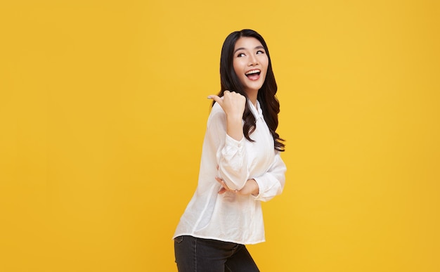 Happy young Asian woman standing with her finger pointing isolated over yellow banner background with copy space.