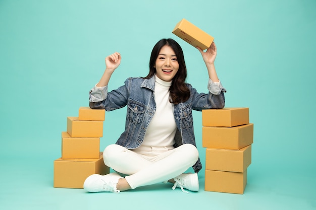 행복한 젊은 아시아 여성 창업 중소기업 프리랜서 소포 상자와 함께 바닥에 앉아 녹색 배경, 온라인 마케팅 포장 상자 배달 개념