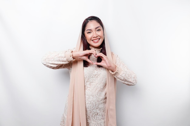 A happy young Asian woman wearing headscarf feels romantic shapes heart gesture expresses tender feelings