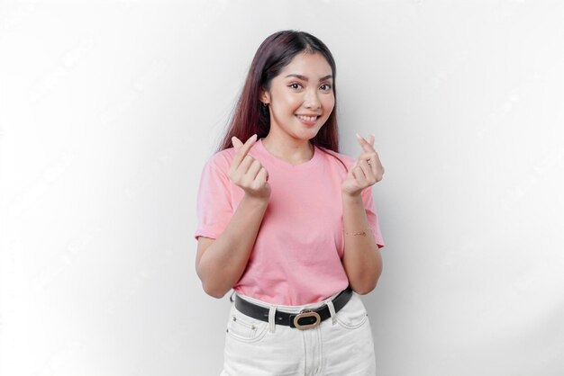 Photo a happy young asian woman wearing a pink tshirt feels romantic shapes heart gesture expressing tend