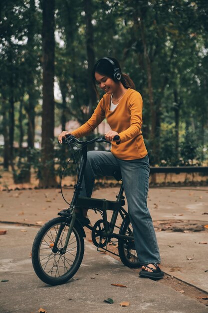 행복한 젊은 아시아 여성이 도시 공원에서 자전거를 타고 있을 때 그녀는 교통의 자전거를 사용하여 미소 짓고 환경 친화적 인 개념