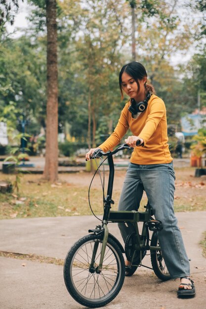 행복한 젊은 아시아 여성이 도시 공원에서 자전거를 타고 있을 때 그녀는 교통의 자전거를 사용하여 미소 짓고 환경 친화적 인 개념