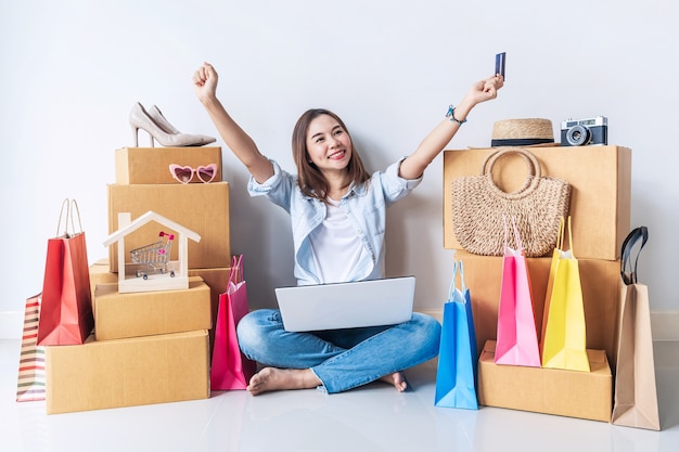 Happy young asian woman with colorful shopping bag and stack of cardboard boxes at home