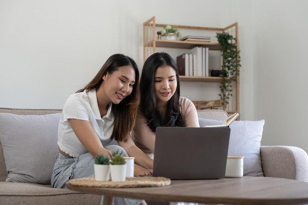 Happy young asian women LGBT lesbian happy couple sitting on sofa using laptop a computer in living room at home LGBT lesbian couple together