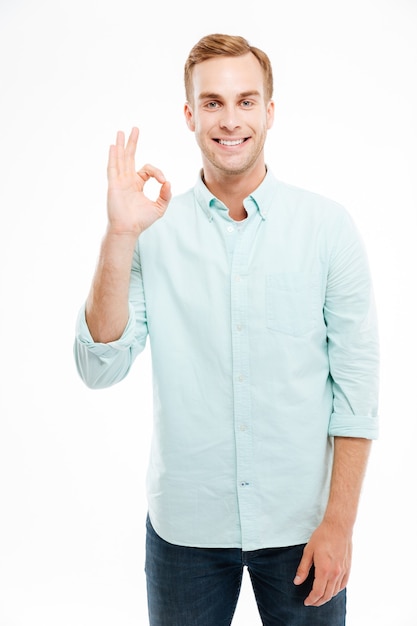 Happy young attractive man showing ok sign with fingers over white wall