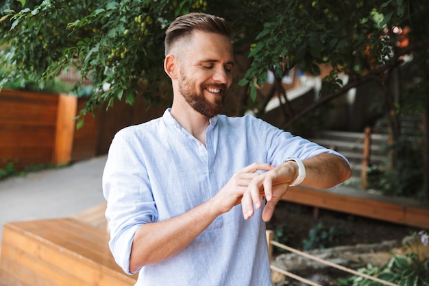 Happy young bearded man looking at his watch.