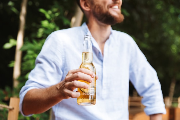 幸せな若いひげを生やした男屋外でビールを飲みます。