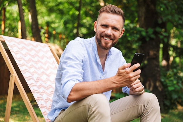 携帯電話を使用して屋外で幸せな若いひげを生やした男。