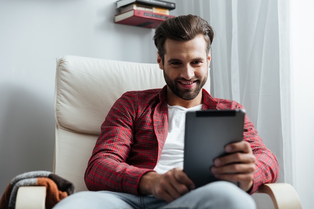 Happy young bearded man using tablet computer.