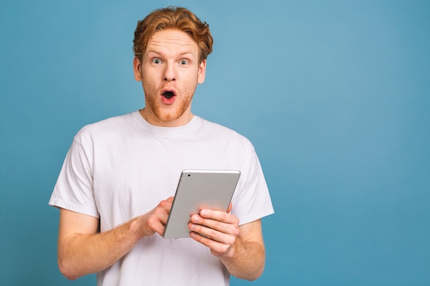 happy young bearded red-haired man in casual using tablet and standing