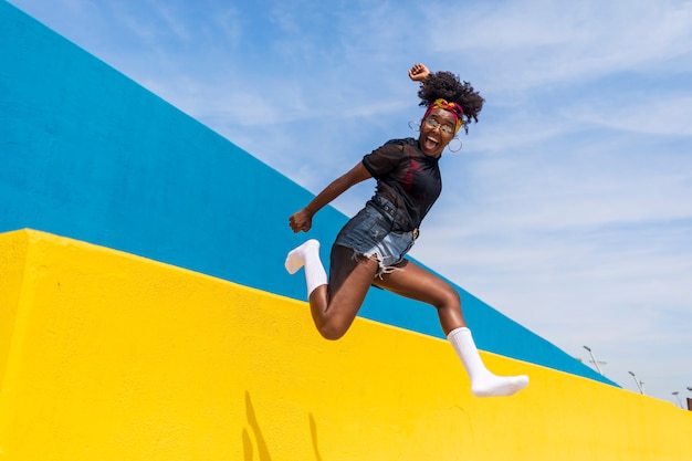 Happy young beautiful afro american woman jumping against wall while smiling