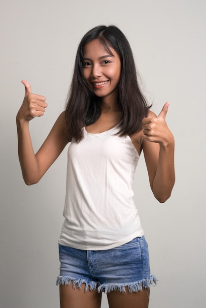 Счастливая молодая красивая азиатская девочка-подросток, показывая палец вверх