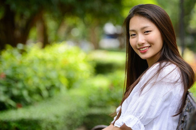 Happy young beautiful Asian teenage woman at the park