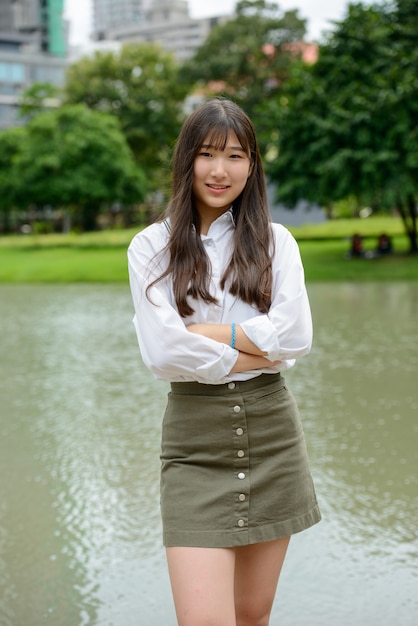 Happy young beautiful Asian teenage woman smiling with arms crossed at the park