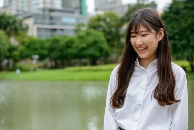 Happy young beautiful Asian teenage woman thinking at the park