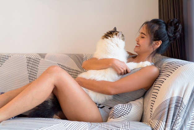 Happy young beautiful Asian woman hugging Persian cat in the sofa at home