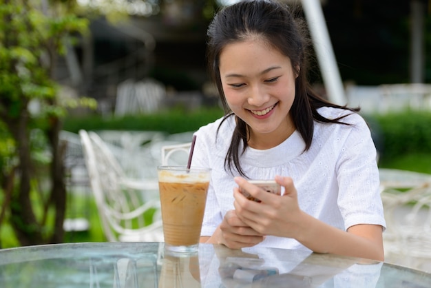 Happy young beautiful Asian woman using phone at the coffee shop outdoors