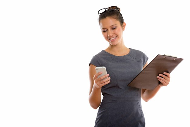 Happy young beautiful businesswoman using phone while holding clipboard