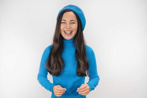 Happy young beautiful girl in blue sweater and beret looking at camera laughing