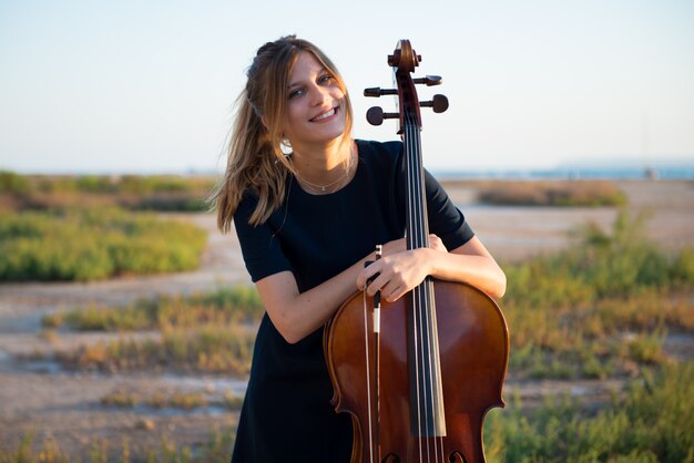 Happy young beautiful girl with her cello on the outside