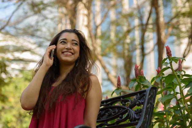 Happy young beautiful Indian woman talking on the phone at the park