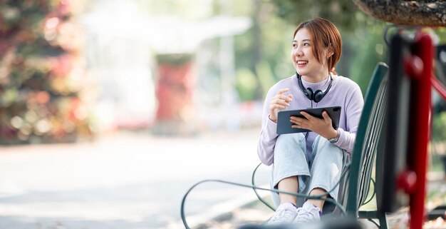 Happy young beautiful student girl sitting outdoors in nature park using laptop computer