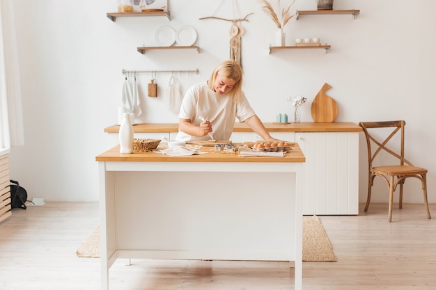 Happy young beautiful woman housewife baker rolls out dough on the kitchen table